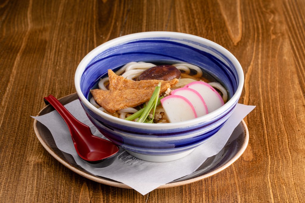 A bowl with thick flour noodles, chicken, fishcake, and vegetables in dashi
